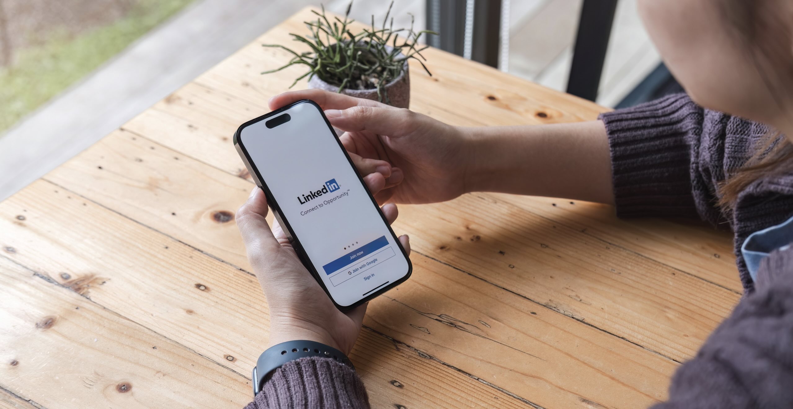 A view of a person's hands holding a smart phone viewing the LinkedIn homepage.