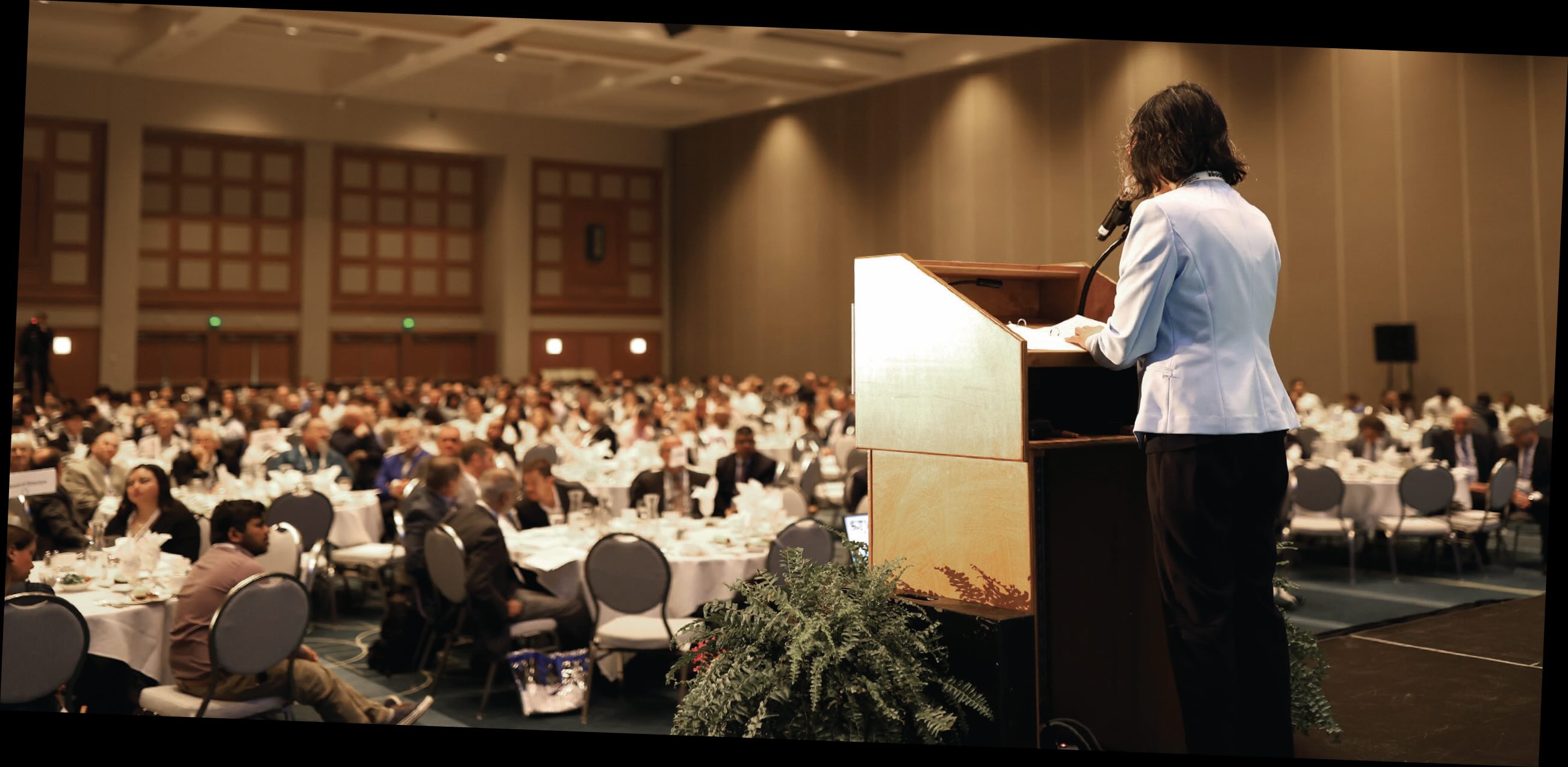 A woman speaks at the podium in front of a large audience.